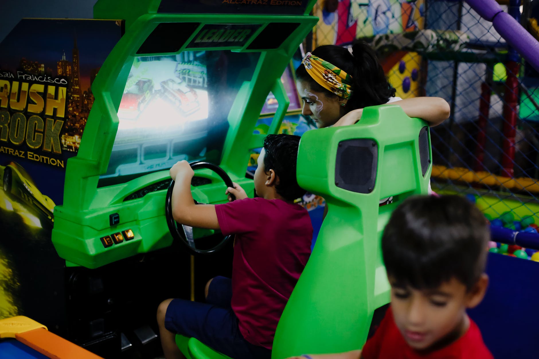 anonymous boy playing car racing simulator near mother and sibling